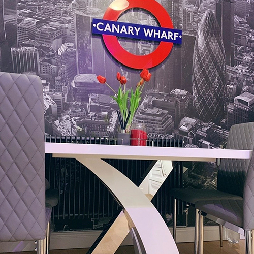 wall covered with aerial drone photo of central london in grey tone. Large bright Canary Wharf london underground sign in centre. White and chrome dining table with 4 grey leather chairs. 