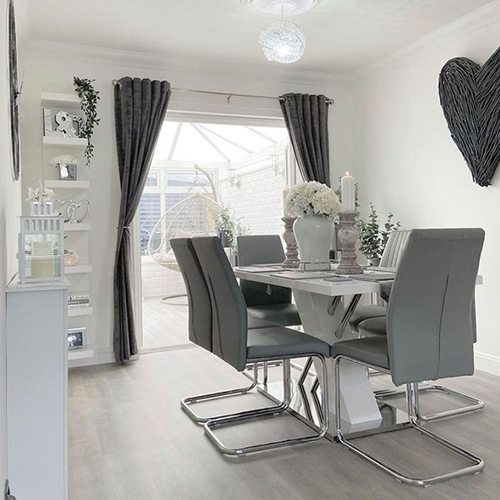 instagram image showing modern dining area - pale floor, white walls and dark grey accessories, with white and chrome dining table and 6 grey faux leather chairs