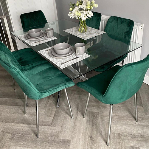 dining area - pale herringbone wood effect floor, grey wall, rectangular glass and chrome dining table with 6 green velvet chairs. 