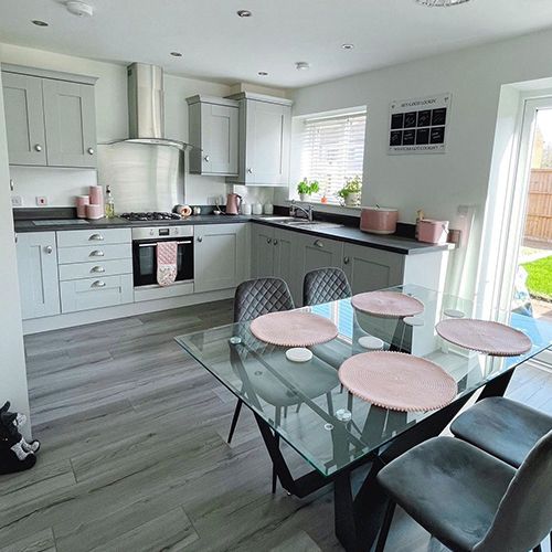 open plan kitchen dining area - pale wood effect floor, grey cabinets rectangular glass and black metal dining table with 4 grey velvet chairs. 