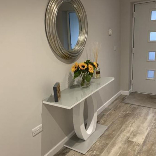 Beige walla dn warm wooden floor in entrance hall. grey and white high gloss console table with feautre halo central plinth, under rounde silver framed mirror. 
