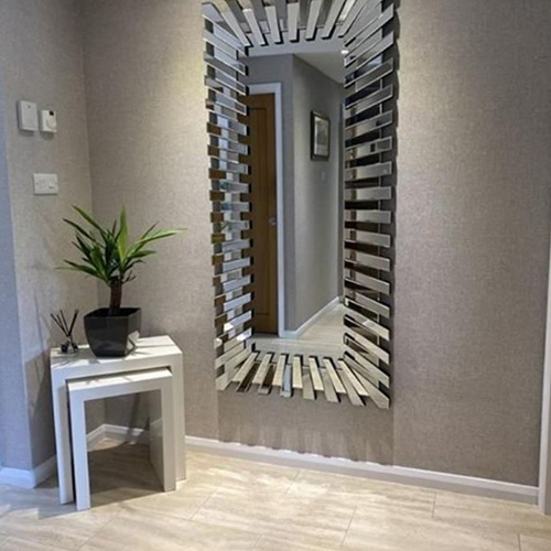 grey walls and pale wood floor hallways with nested white square tables in corner, with potted plant on top. Large long starburst rectagular mirrow veritcal on wall behind