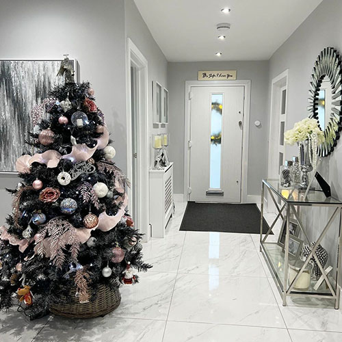 Bright modern entry hallway with white walls and tiles floor, dressed for Christmas - christmas tree in left of frame. Hallway featres Regent glass and chrome console table and Starburst round wall mirror. 