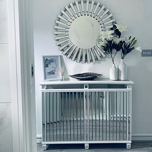 Entrance hallway  - mirrored radiator cover with shelf top sporting artwork, dish and vases with flowers, and large Starbusrt round mirror on wall behind.