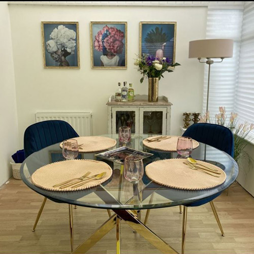 glass round dining table with gold legs, blue velvet chairs with gold legs, navy, gold and pink accessories/tableware that matches artwork on the wall