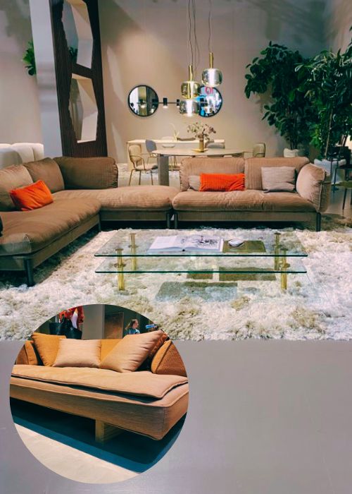 oversized living room furniture - low and wide/deep sofa with warm brown neutral velvet and pops of orange in cushions, with large but low glass coffee table that has gold legs, on shagfgfy rug. Inset of a second wide and low sofa. 