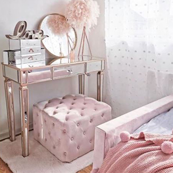 mirrored console table used as a dressing table in a sunlit bedroom, with pink velvet stool and pink accessories.