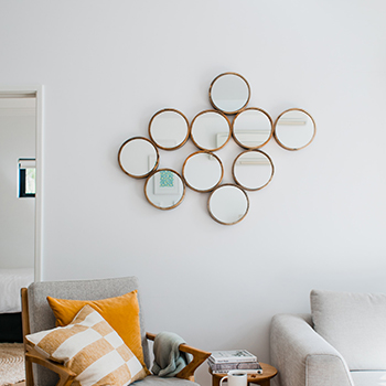 Gallery mirror wall ideas - modern simple living room with a mirror gllaery wall comprising of 10 small round mirrors all identical and connected, in thin gold frames.