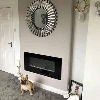 A modern living room with neutral colours. A modern fireplace. A round mirror in starburst frame is hung above the fireplace.