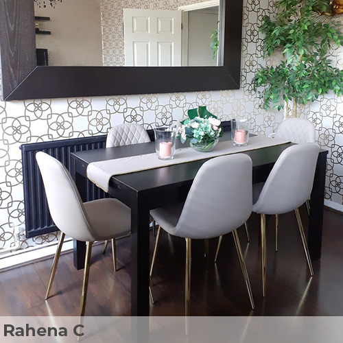 modern dining area with drk but warm toned wooden flooring, black simple table with 6 white faux leather dining chairs with gold legs (Corona chairs from Furniturebox UK). White wall with gold geometric pattern. Large black frame mirror and green pot plants. 