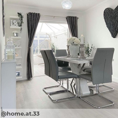 instagram image from @home.at.33 featuring white gloss and chrime dining table abd 6 grey faux leather cantilever chairs with chrome legs. In dining room with white walls, pale wood laminate flooring and white and grey accessories.