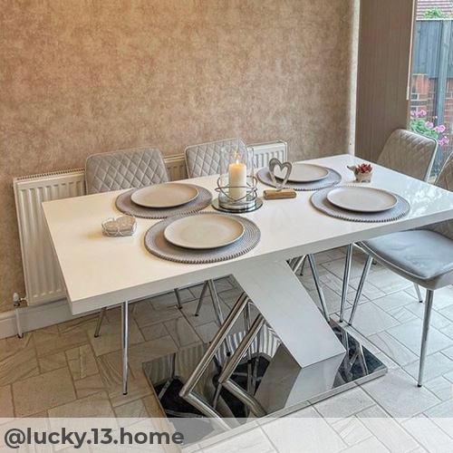 Instagram image from @lucky.13.home. Warm dining room with mottled terractotta and beige wall, and abstract textred pale grey/cream tile flooring. Large white gloss and chrome dining table with 4 grey velvet chairs. 