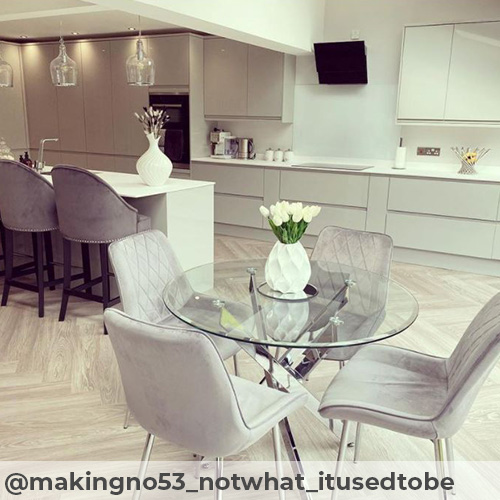 Instagram image from @makingno53_notwhat_itusedtobe. Bright modern kitchen-dining area with light coloured herringbone flooring. Featuring white counters in background and round glass dining table with chrome legs and 4 grey velvet chairs in foreground.