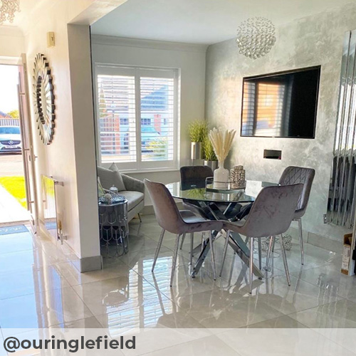 Instagram image from @ouringlefield. Bery modern and glossy open plan dining area featuring high gloss marble effect floor tiling and glass and chrome dining table, with 4 grey velvet chairs. 