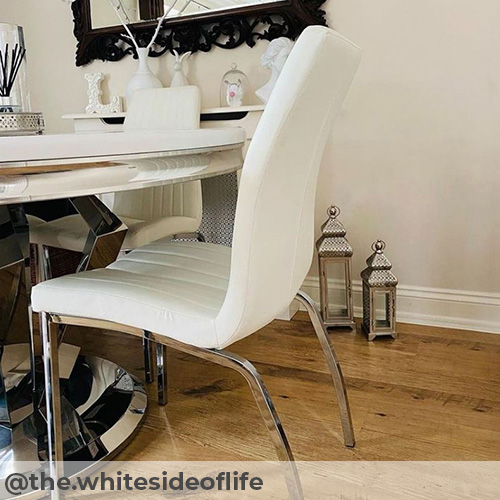 instagram image from @the.whitesideoflife - modern dining area. warm but light coloured wooden flooring with white gloss nad chrome dining table and white Isco dining chairs for Furniturebox UK. An ornate black gramed mirror hands above a radiator cover in the backgrond, with white christmas ornaments, and silver lanterns placed on the floor. 
