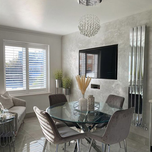 bright modern grey dining room with round glass dining table and 4 grey velvet chairs