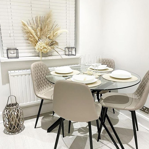 round glass dining table with black hairpin legs and 4 faux leather beige chairs with black legs in scandi dining room