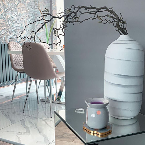 modern dining area - grey wall in foreground with grey and pink marbled wallpaper in background, and corner of white high gloss table with beige faux leather chairs that look pinky against wallpaper