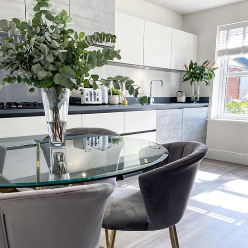 grey and white kitchen diner area with round glass dining table with gold legs and grey velvet chairs