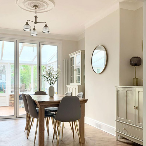 cream and wood dining area with wooden farmhouse table and 6 grey faux-leather dining chairs with gold legs. 