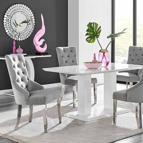studio shot of white high gloss table with 4 grey velvet knockerback style dining chairs with lots of pink accessories