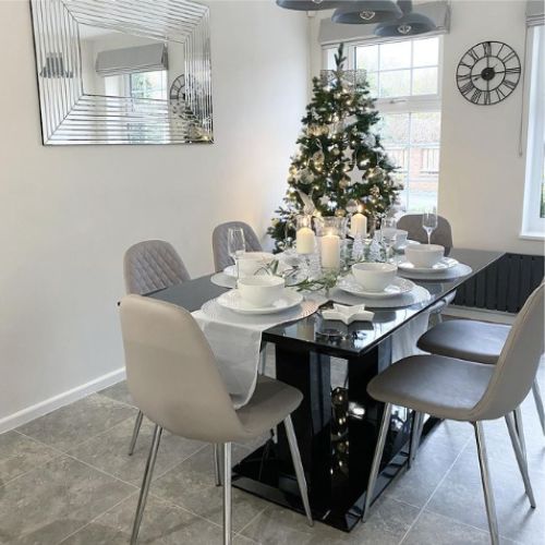 black high gloss dining table with 2 pilar legs, 6 grey faux leather chairs with silver legs, table runner, dressed for Christmas, gold and silver tree in background
