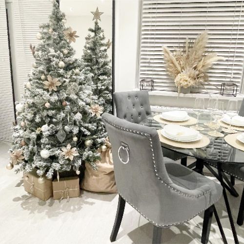 round glass dining table with black hairpin legs, grey knockerback dining chairs, beige and gold table wear, silver and gold christmas tree