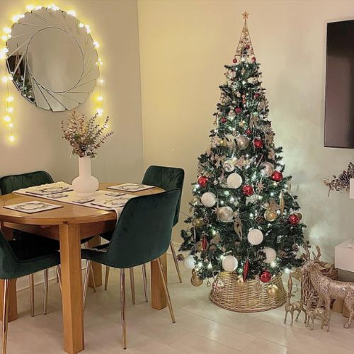 round wooden dining table and 4 green velvet chairs with gold lets, with christmas tree and round wall mirror in background