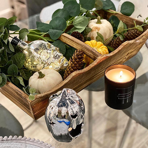 glass dining table with wooden trug tray filled with green leaves, glass skulls and pukins with fiary lights