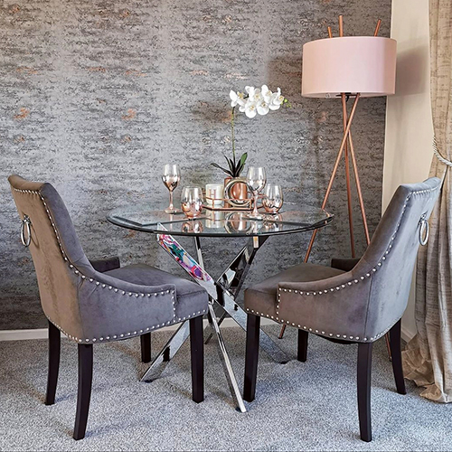 modern dining area showing glass dining table and grey velvet chairs, with rose gold dining table centrepieces on the table
