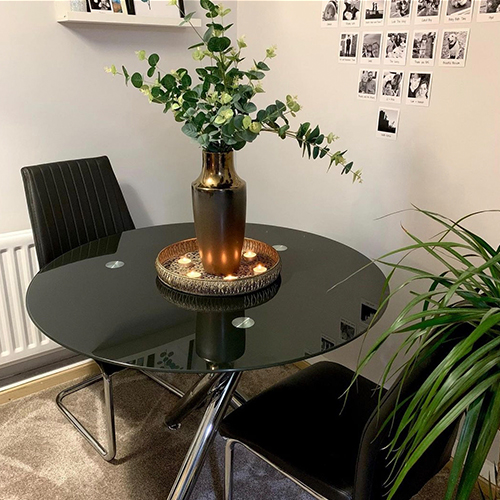 round black glass table with 2 black chairs, copper bowle with tealights around a tall copper vase filled with tall sticks of greenery/leaves