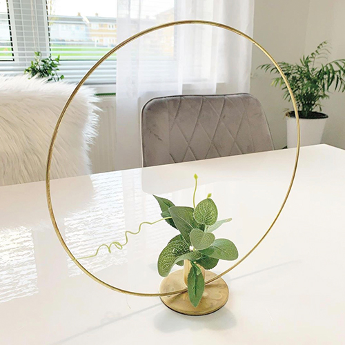 white gloss table with grey velvet chairs, with small leafy psy in a small gold vase that has a round halo structure around it.
