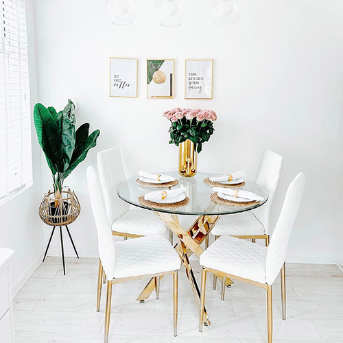 round glass table with gold starbusrt legs, 4 white faux leather chairs with gold legs. Tall gold vase with pink roses
