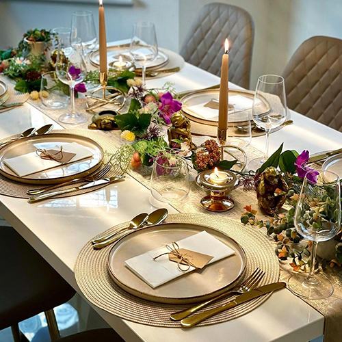 white high gloss table with colourful tablescape of coloured candles, flowers, fruits and gold brass ornaments