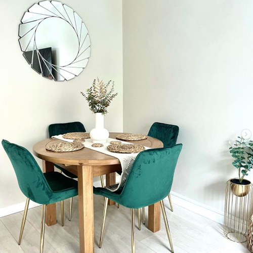 round wooden table with 4 green velvet chairs, with white vase filled with dried grasses, leaves and corn.