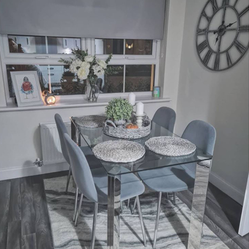 grey dining room with glass and chrome table and grey woven basket with green plant and grey candles.