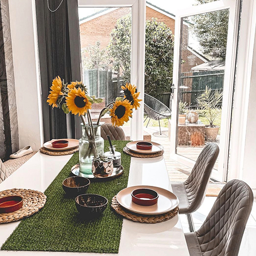 glass vase of sunflowers on a modern dining table, vase sat on a green astroturf style table runner