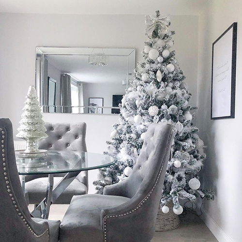 round glass dinin table with small white christmas tree centrepiece and large decoarted christmas tree in the background. 