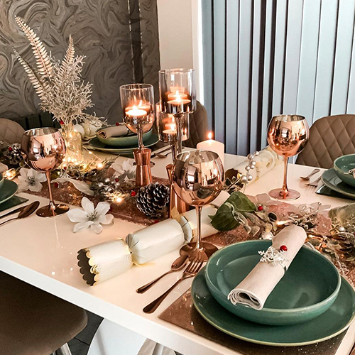 table dressed for christmas, with rose gold themed tablescape featuring cnagles, glasses, pinecones, berries,