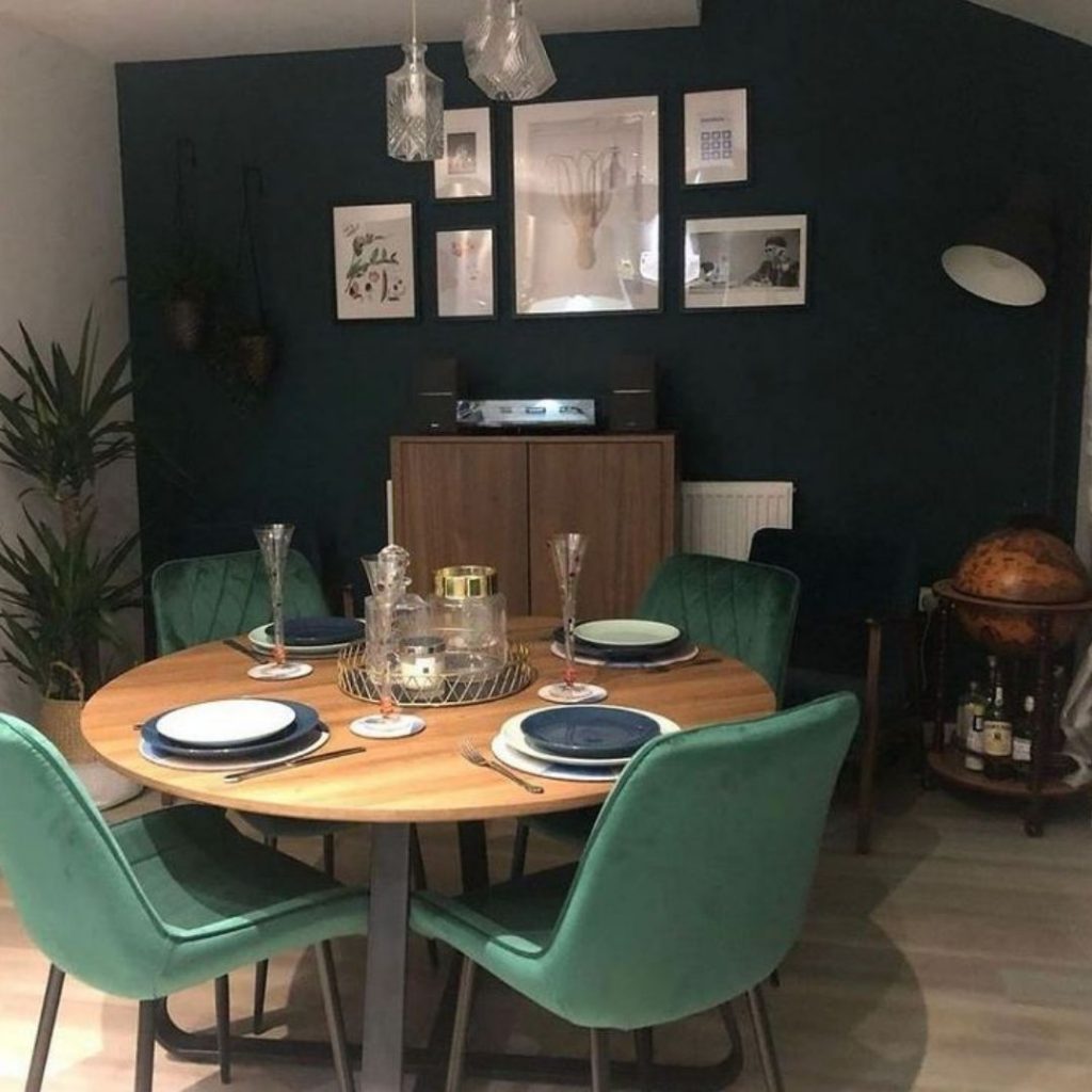 Customer image of the Furniturebox UK Santorin brown round dining table with matt black metal curved legs, in a modern dining room, with 4 green velvet Pesaro dining chairs place around it