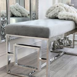 grey velvet statement bench on silver chrome art deco geometric frame legs, in front of large statement ornate silver wall mirror. Chunky white knit throw placed on bench.