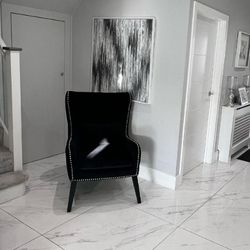 black velvet wingback chair with silver studs placed in alcove at bottom of stairs on white marble tiled flooring.
