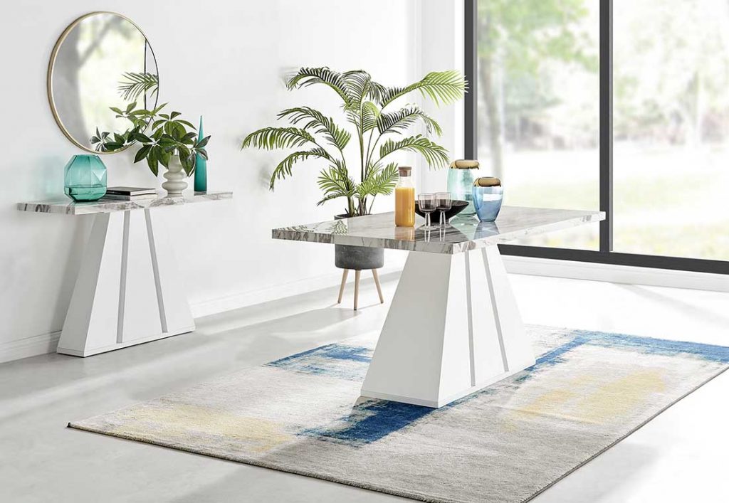 statement dining table with marble-effect top and ancient greece inspired plinth leg. Sits on blue and yellow rug, with matching console in the background. 