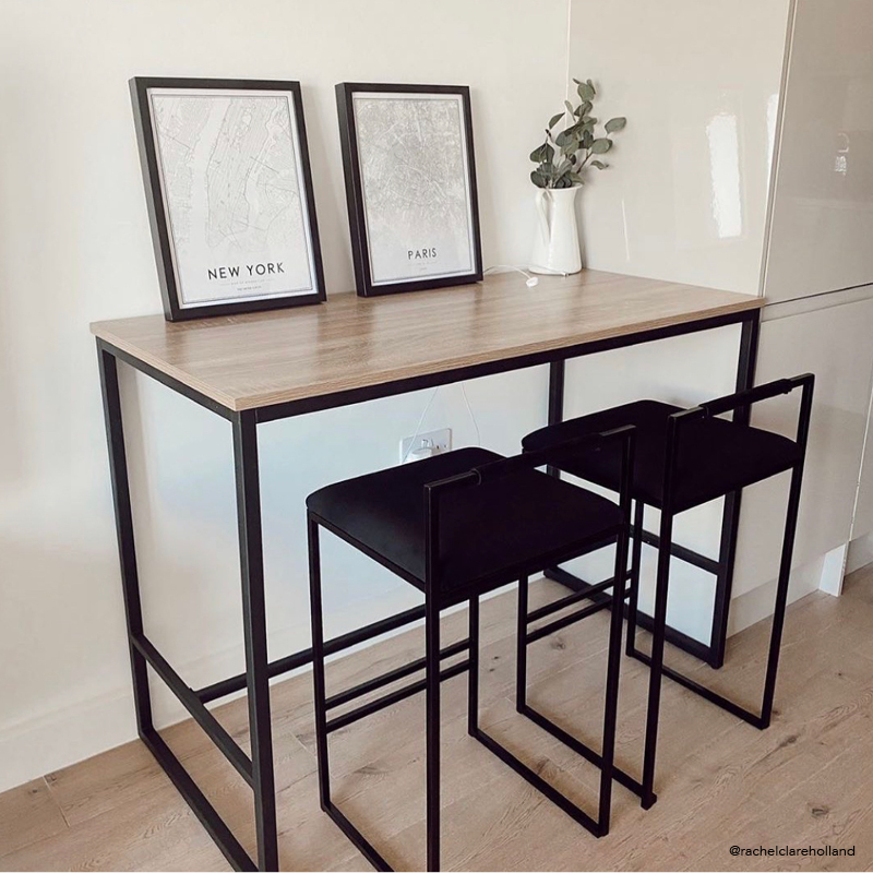 A stylish black and wooden bar table against a wall