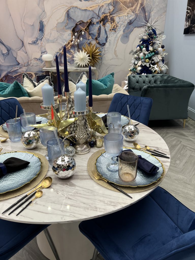 Christmas dining space with white marble effect round dining table and navy blue velvet chair. Decorated with gold and silver stars and celestial theme.