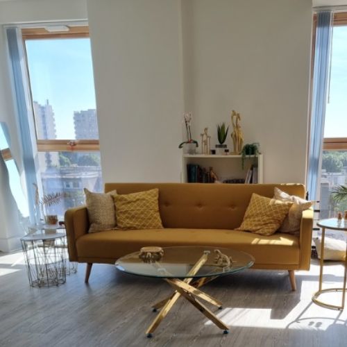 modern bright living room space with mustard yellow fabric sofa, yellow cushions and round glass coffee table. Cosy home ideas with yellow tones throughout