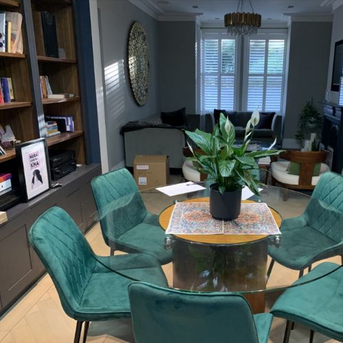 modern open plan kitchen diner with tal bookcase, round glass dining table, green velvet dining chairs, sofa in background