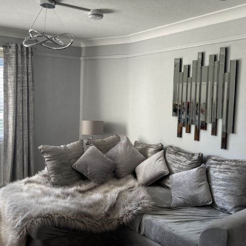 modern grey living room with grey velvet sofa and throws, abstract wall mirror on wall