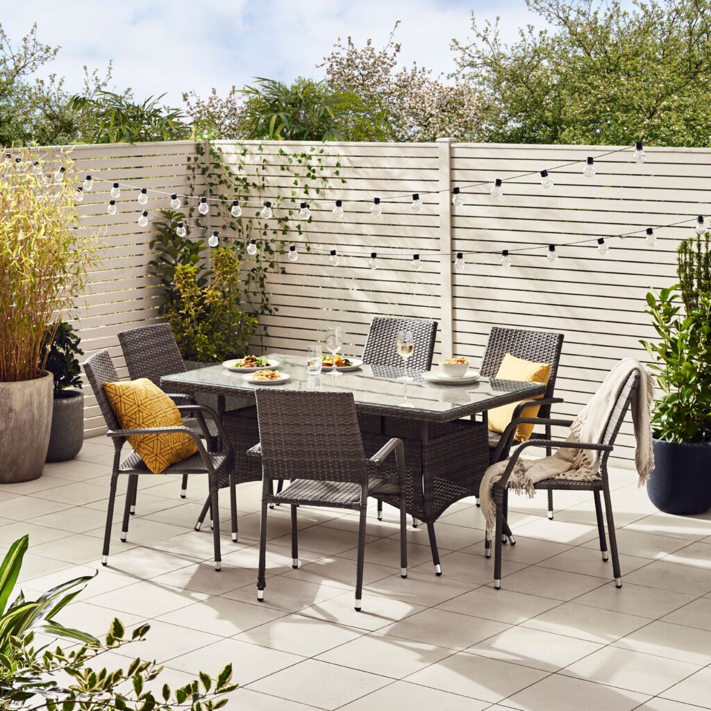 brown rattan garden dining table and chairs in modern garden setting with plants and fencing