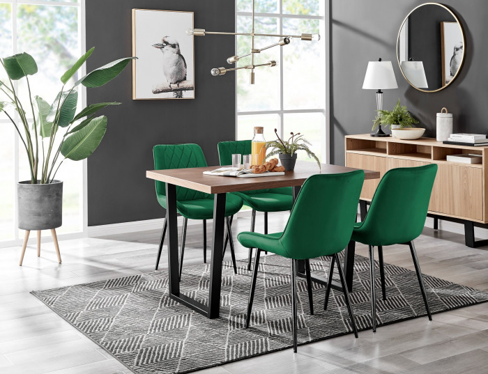 A wooden dining table with green dining chairs in a modern dining room with grey walls and large plant